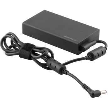 Schrägansicht des schwarzen XMG / SCHENKER 240 Watt Netzteils mit angeschlossenem Kabel, Ferritkernen und gewinkeltem DC-Hohlstecker.