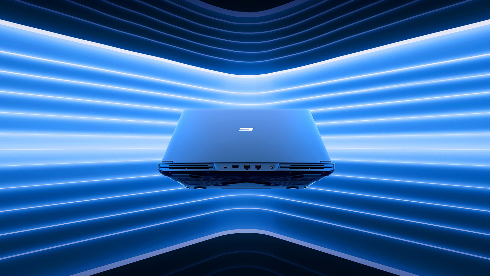Ein geschlossener XMG Gaming-Laptop vor futuristischer blauer LED-Hintergrundbeleuchtung mit sichtbaren Anschlüssen.