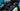 Gamerin sitzt an einem High-End-Setup mit Gaming-Laptop, beleuchteter RGB-Tastatur, Monitor und Gaming-Headset.