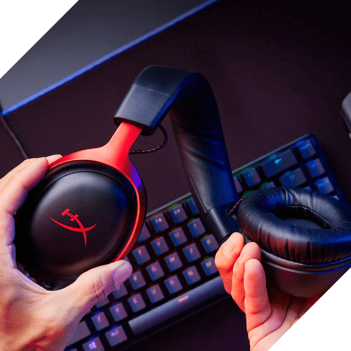 Schwarzes Gaming-Headset mit roten Akzenten und HyperX-Logo wird über einer mechanischen Tastatur gehalten.