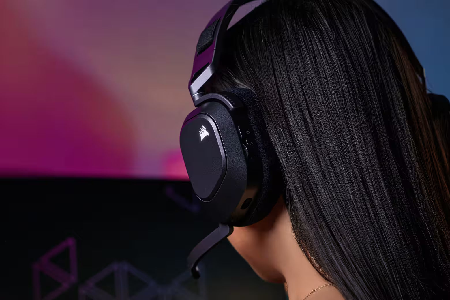 Person mit langen dunklen Haaren trägt ein schwarzes Corsair Gaming-Headset vor RGB-Beleuchtung.