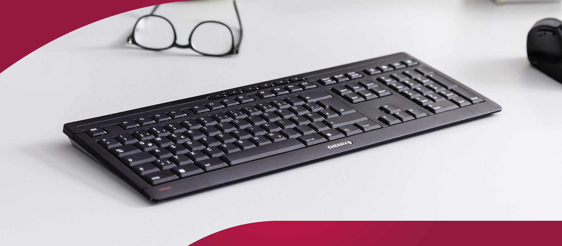 Schwarze Cherry-Tastatur auf hellem Schreibtisch mit Brille und Maus