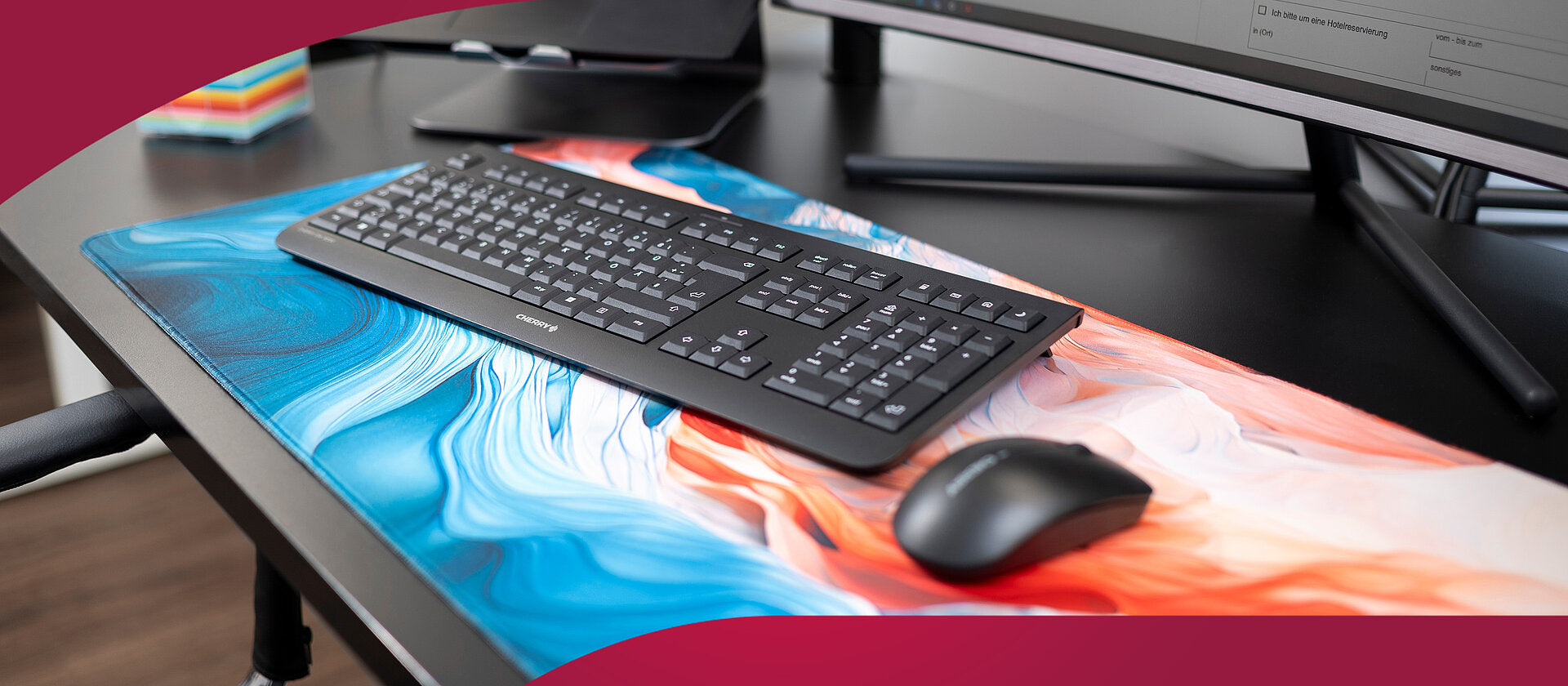 Schwarze Cherry Tastatur und Maus auf einer großen, blau-orangen Gaming-Mauspad auf einem Schreibtisch.