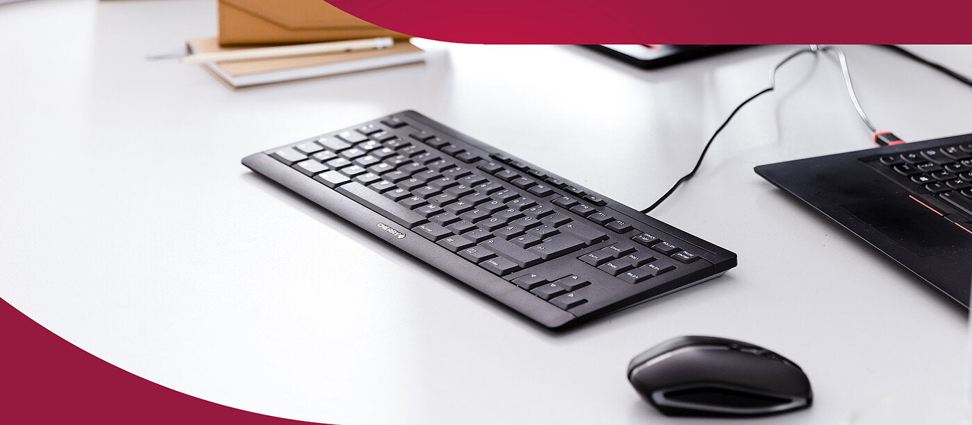 Schwarze Cherry Tastatur und Maus auf einem hellen Schreibtisch neben einem Laptop
