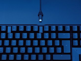Nahaufnahme einer beleuchteten Laptop-Tastatur im blauen Licht mit angeschlossenem USB-C-Kabel.