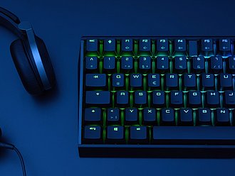 Nahaufnahme einer Gaming-Tastatur mit RGB-Beleuchtung und Gaming-Headset auf dunklem Schreibtisch