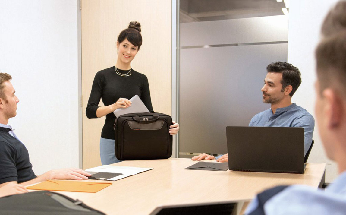 Frau packt ein Business-Laptop in eine schwarze Notebooktasche während eines Meetings in einem modernen Büro.