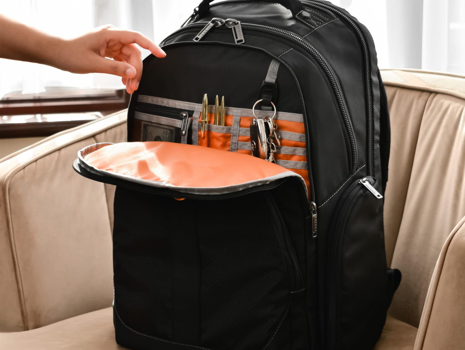 Schwarzer Laptop-Rucksack mit geöffnetem Fach und orangem Innenfutter für Hardware und Zubehör.