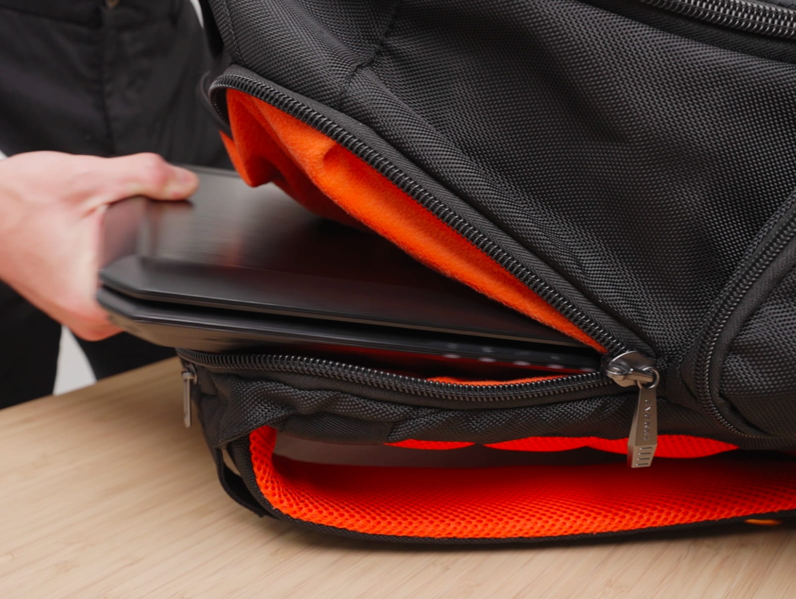 Schwarzer Gaming-Laptop wird in den orange gefütterten Rucksack gesteckt
