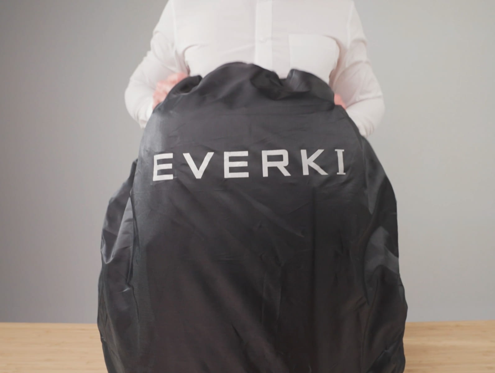 Person in weißem Hemd hält einen schwarzen EVERKI Staubschutzbeutel auf einem Holztisch.
