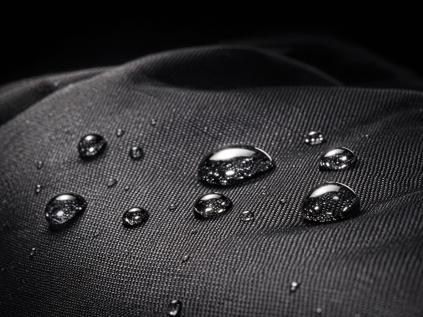 Wassertropfen perlen von der wasserabweisenden Oberfläche eines schwarzen Laptop-Rucksacks ab.