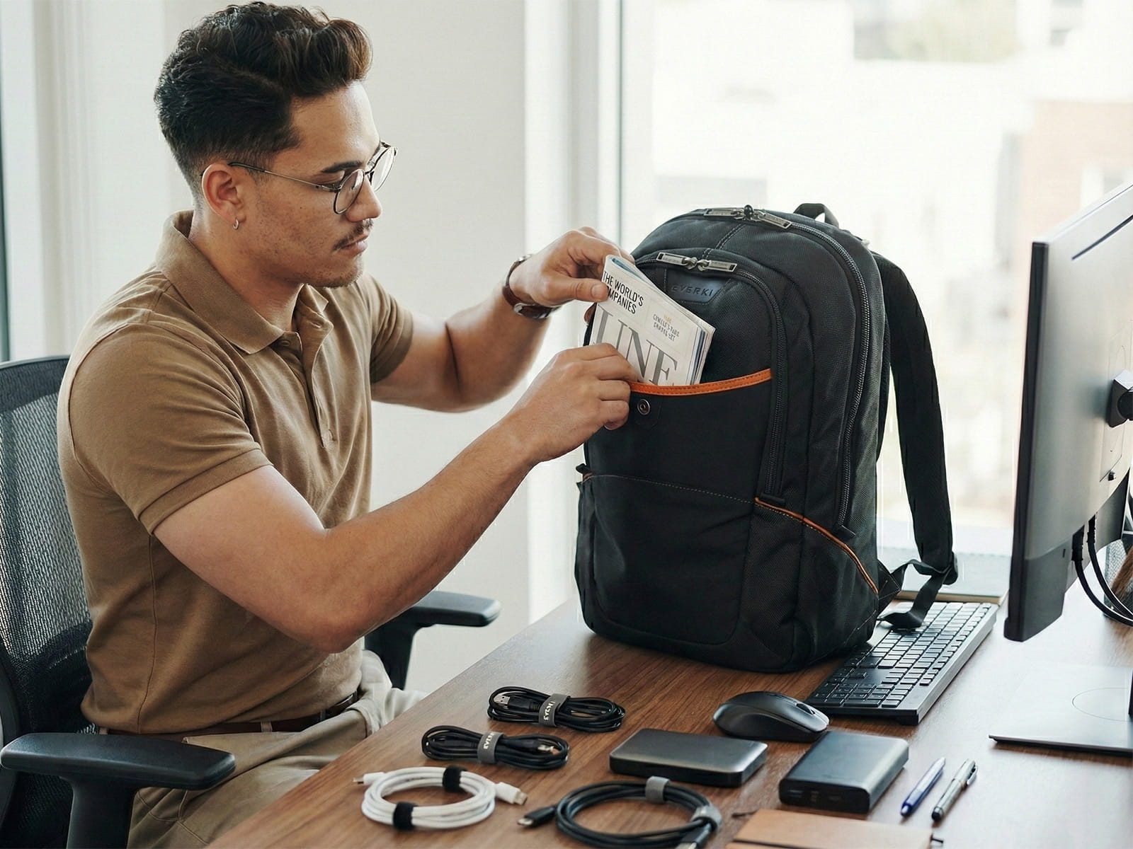 Mann packt einen Everki Laptop-Rucksack an einem Schreibtisch mit IT-Zubehör und Kabeln aus.