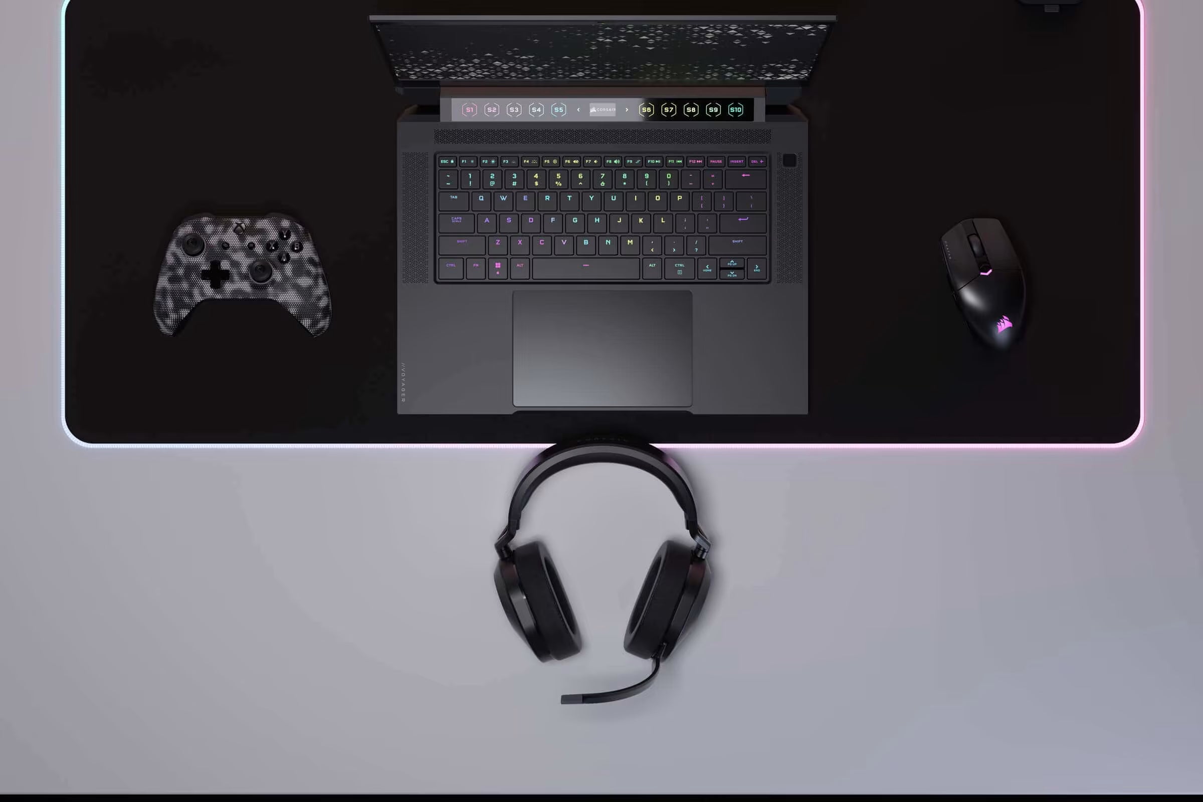 Gaming-Setup aus der Vogelperspektive mit Corsair Laptop, beleuchteter Maus, Controller und Headset.