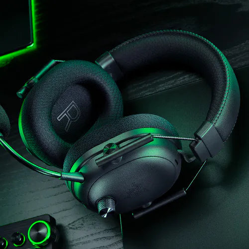 Schwarzes Gaming-Headset mit grüner Akzentbeleuchtung und Mikrofon auf dunklem Tisch