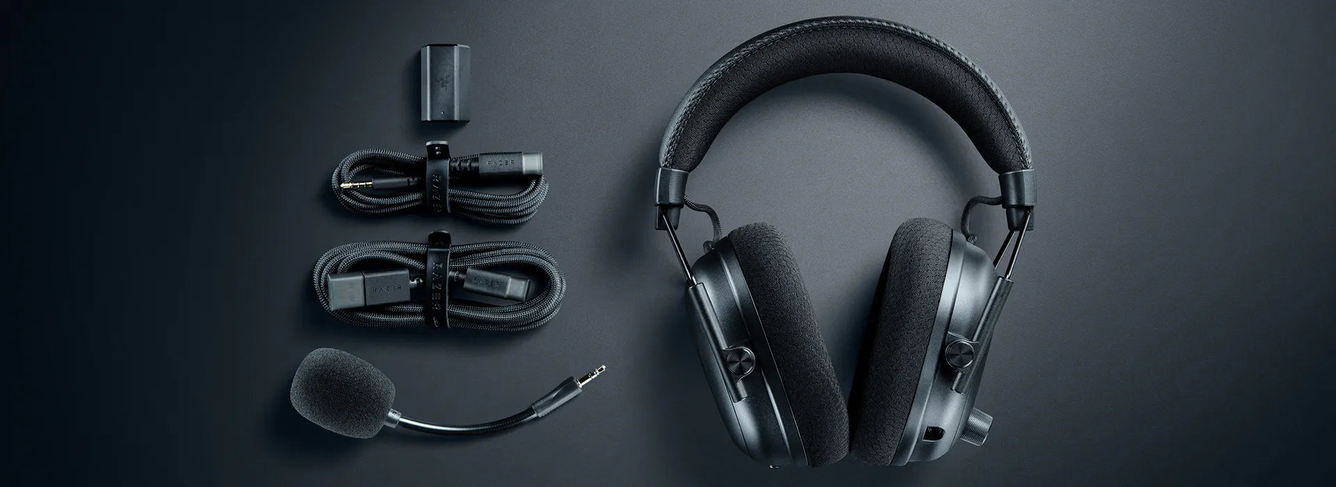 Schwarzes Gaming-Headset mit abnehmbarem Mikrofon und Zubehörkabeln auf dunklem Untergrund