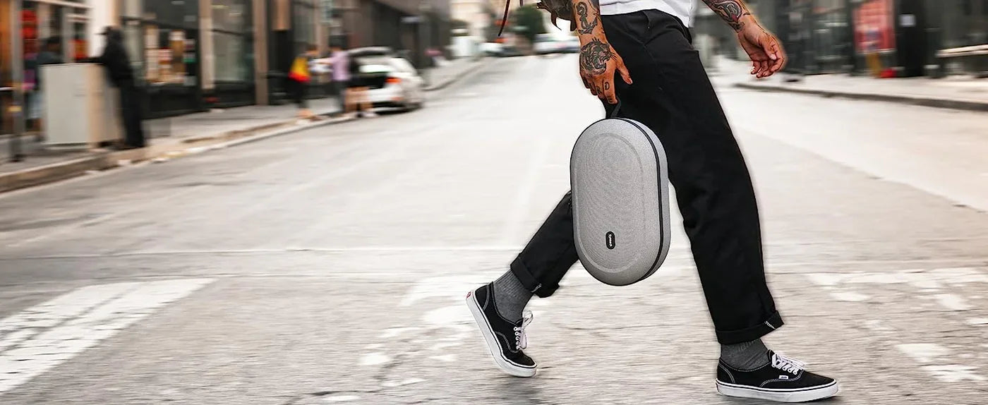 Person geht mit grauer VR-Headset-Transportbox in der Hand über eine Straße.