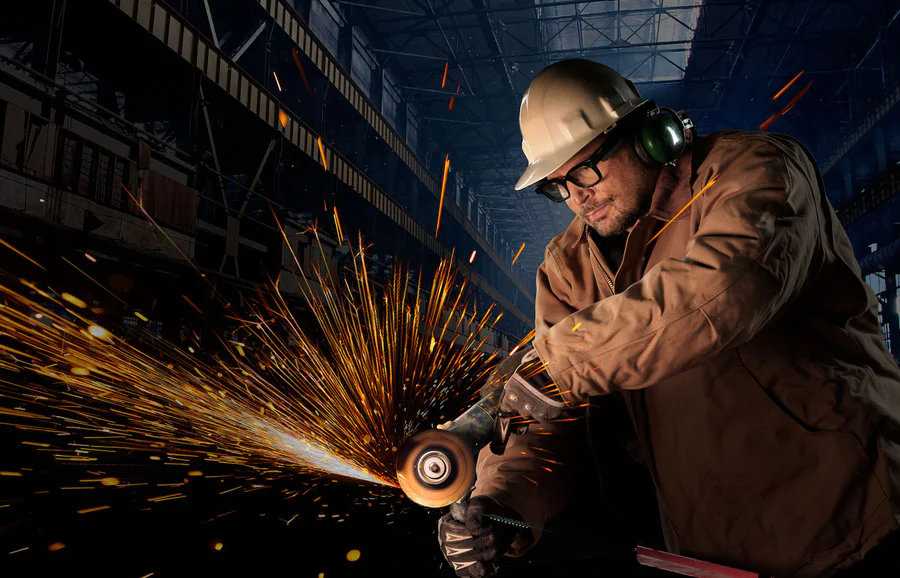 Handwerker mit Schutzhelm und Gehörschutz arbeitet mit einer Flex, wobei viele helle Funken fliegen.