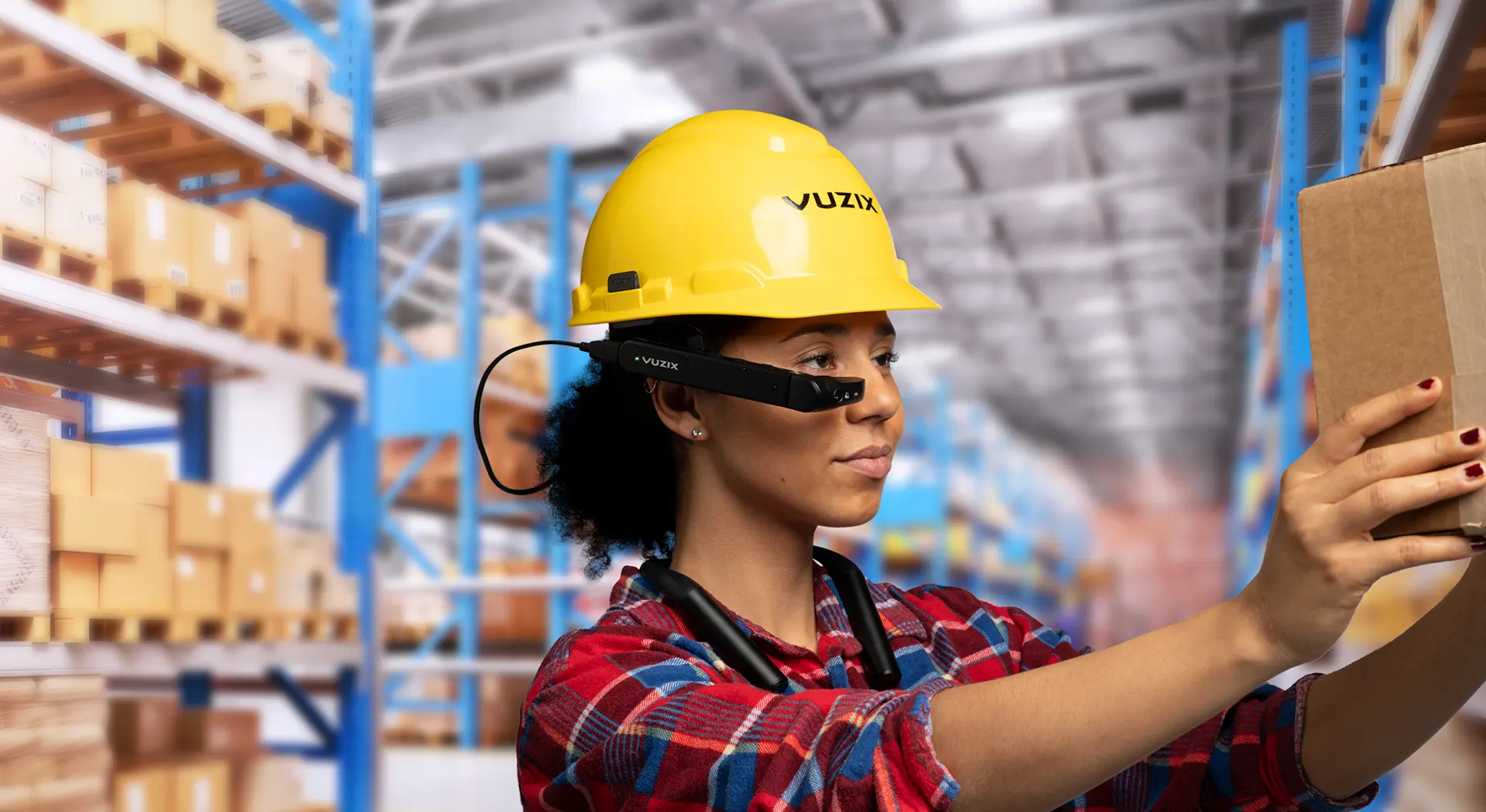 Lagerarbeiterin mit gelbem Helm trägt Vuzix Smart Glasses und scannt Karton