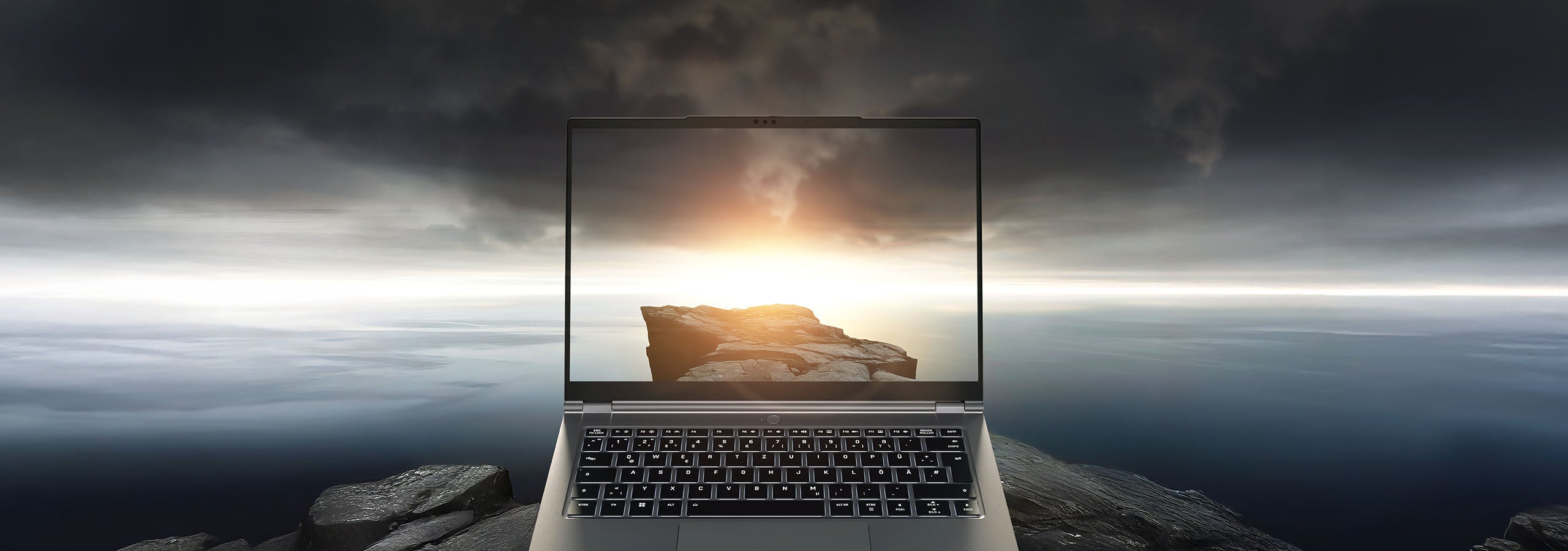 High-End Laptop auf felsiger Klippe mit dramatischer Meereslandschaft und Sonnenuntergang auf dem Display