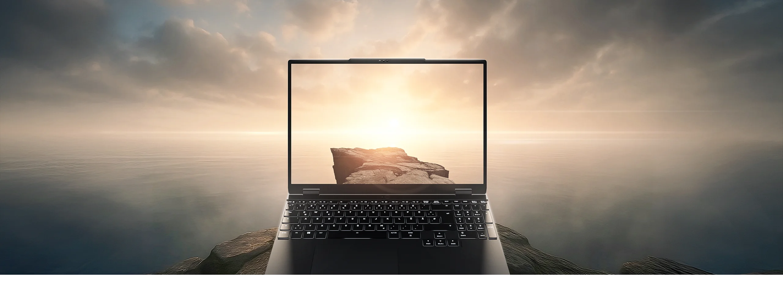 High-End Laptop auf einer felsigen Klippe am Meer bei Sonnenuntergang mit nahtlosem Display-Übergang in die Landschaft.