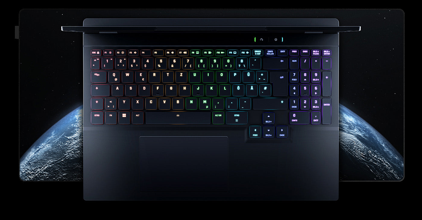 Aufsicht auf die beleuchtete RGB-Tastatur eines Gaming-Laptops mit deutschem Layout vor einer großen Schreibtischunterlage mit Weltraummotiv