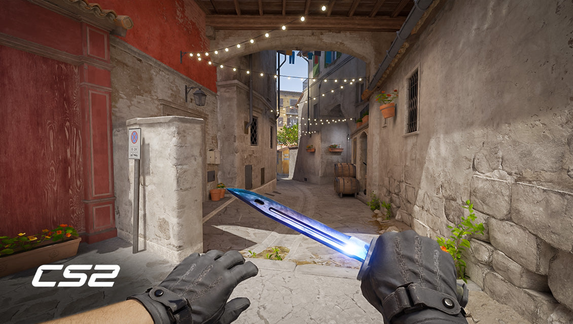 Spielerperspektive in CS2 auf der Map Inferno mit blauen Handschuhen und einem blauen Messer.