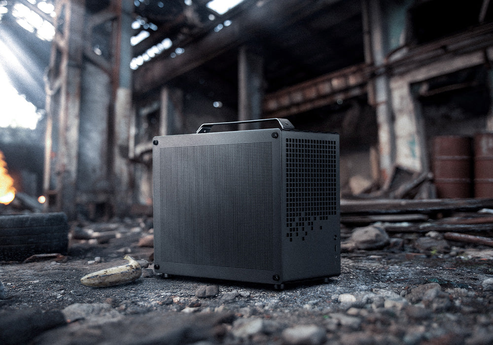 Kompakter High-End Gaming-PC im schwarzen Mesh-Gehäuse mit Tragegriff in einer rauen Industrie-Ruine