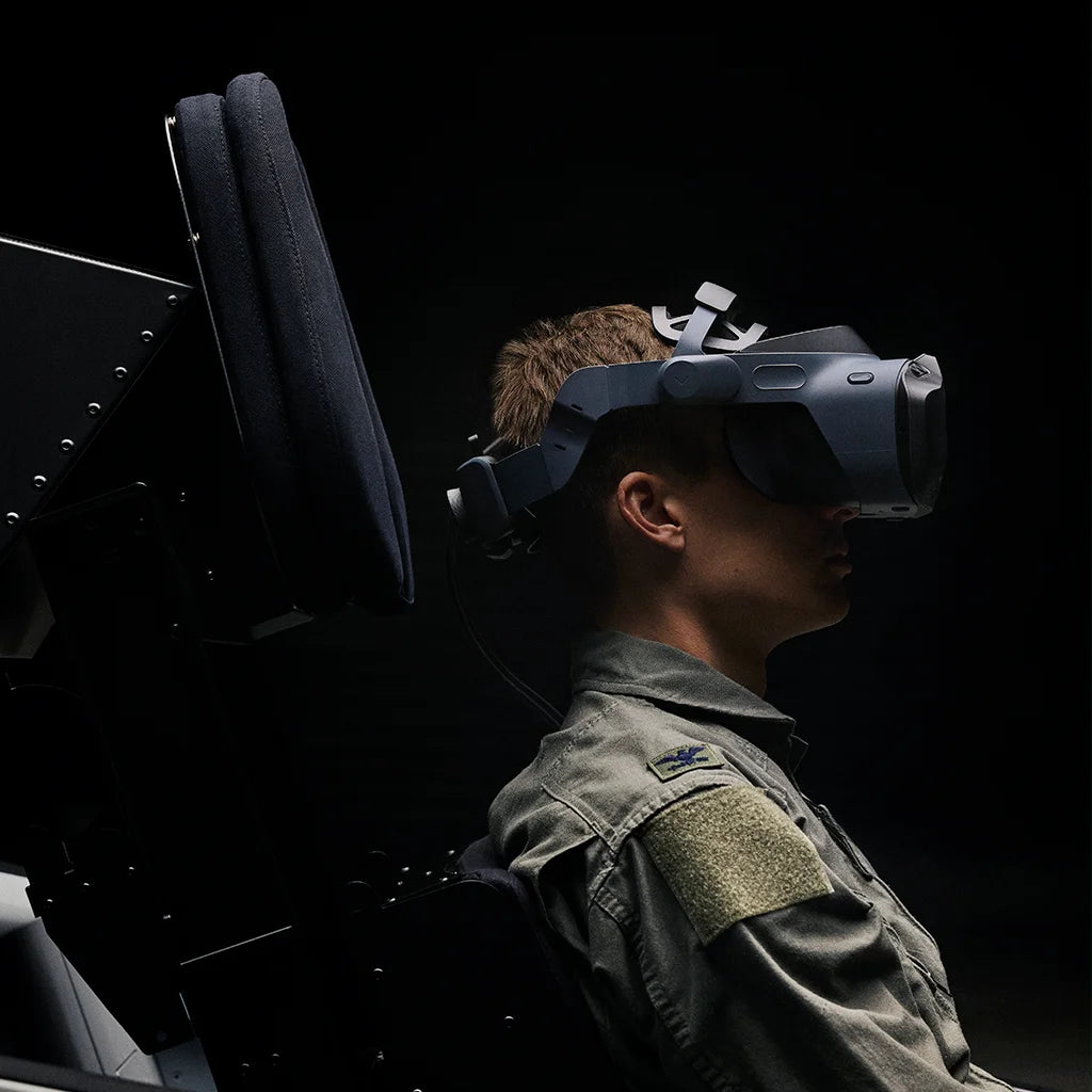 Person mit VR-Headset sitzt in einem Simulator vor dunklem Hintergrund.