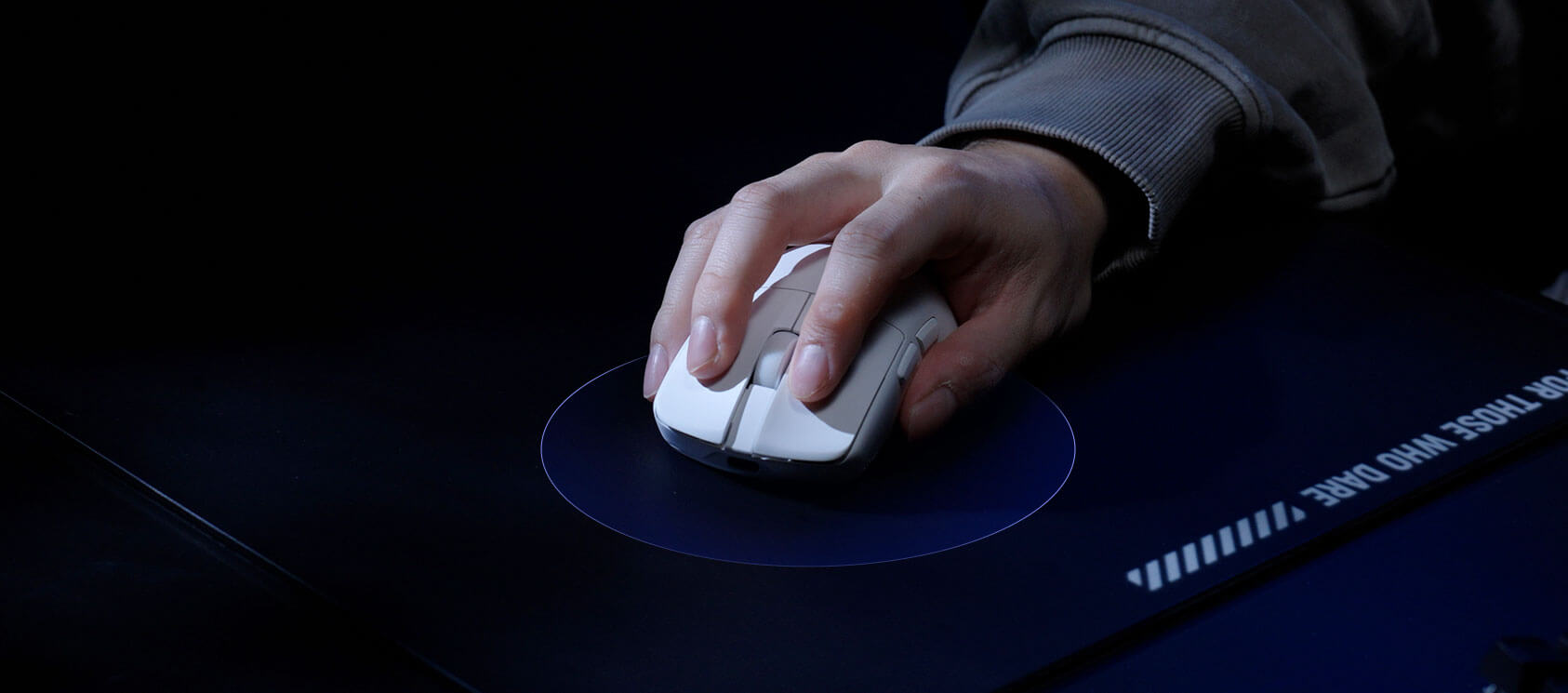 Hand bedient weiße Gaming-Maus auf dunklem Mauspad mit blauem Lichtkreis