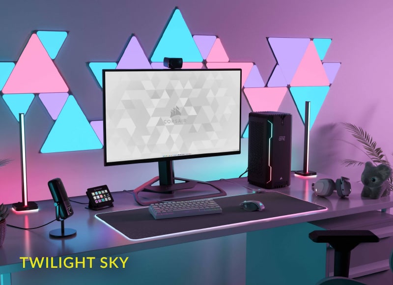 High-End Gaming-Setup mit Corsair PC, Monitor, Tastatur, Maus und dreieckigen Wandpaneelen in Rosa- und Blautönen.