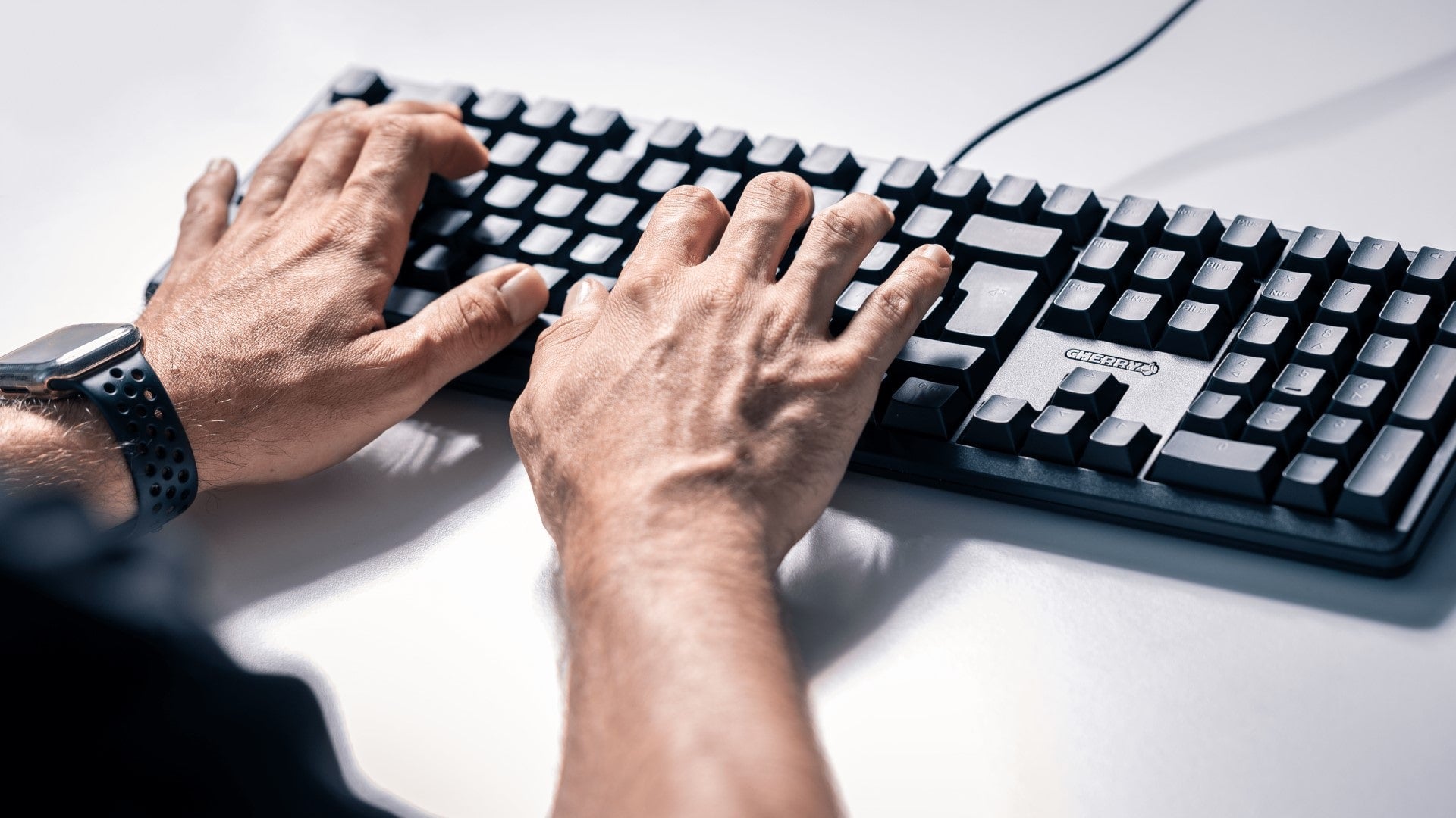 Hände tippen auf einer schwarzen CHERRY-Tastatur auf hellem Schreibtisch