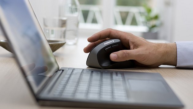 Hand bedient eine ergonomische Cherry-Vertikalmaus neben einem Laptop auf einem Schreibtisch.