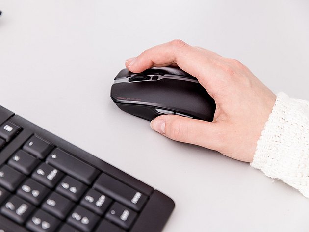 Hand bedient eine schwarze Ergonomie-Maus neben einer Tastatur auf hellem Schreibtisch.