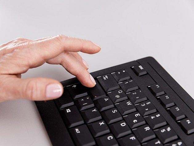 Hand tippt auf die Tasten einer schwarzen Computertastatur
