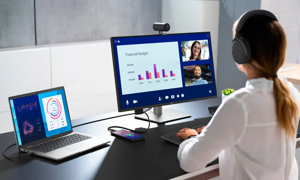 Person mit Headset an modernem Arbeitsplatz mit Laptop, externem Monitor, Webcam und Peripherie.