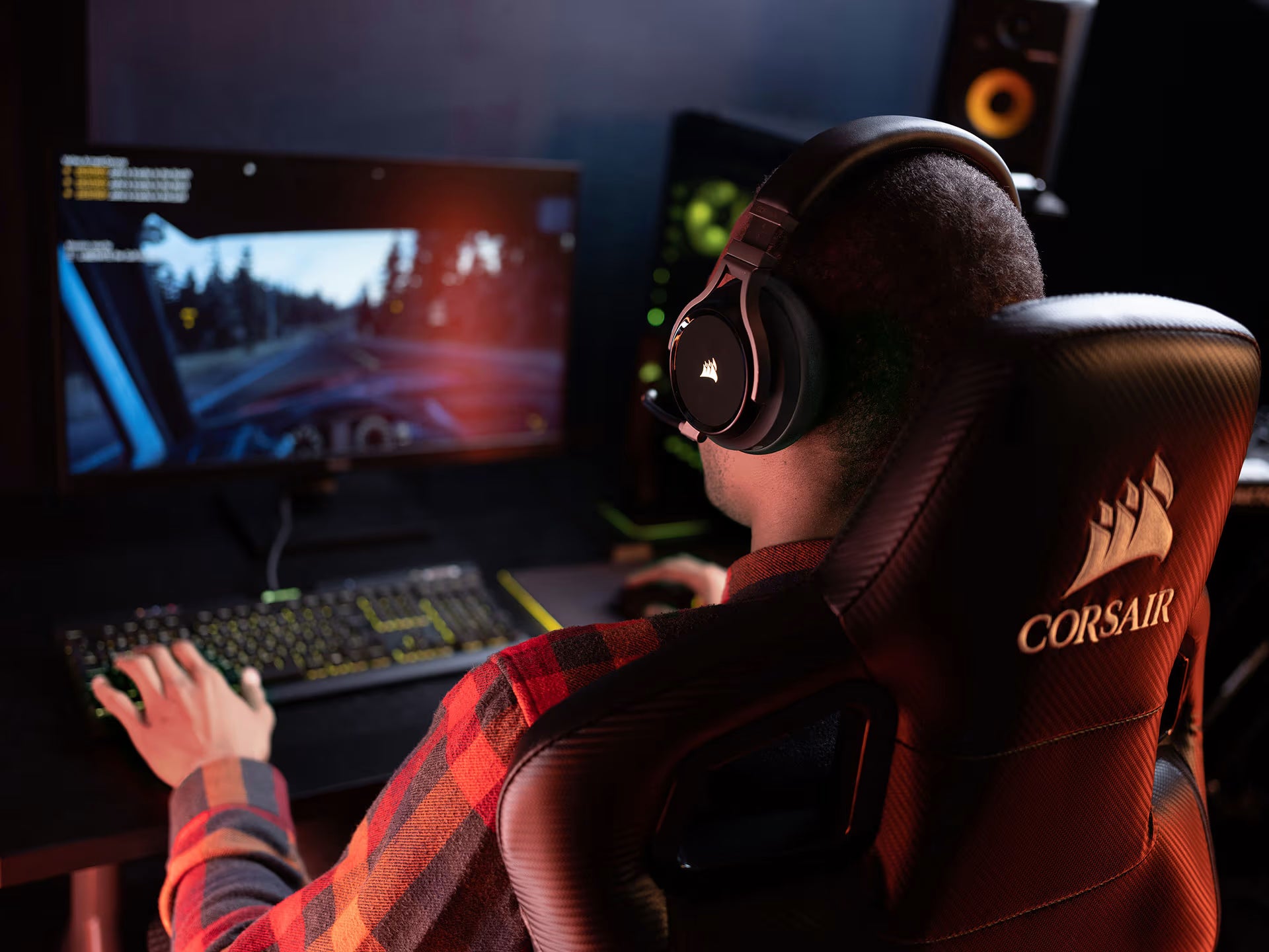 Gamer mit Headset sitzt auf Corsair Stuhl vor Monitor und spielt an High-End Gaming-PC mit RGB-Peripherie