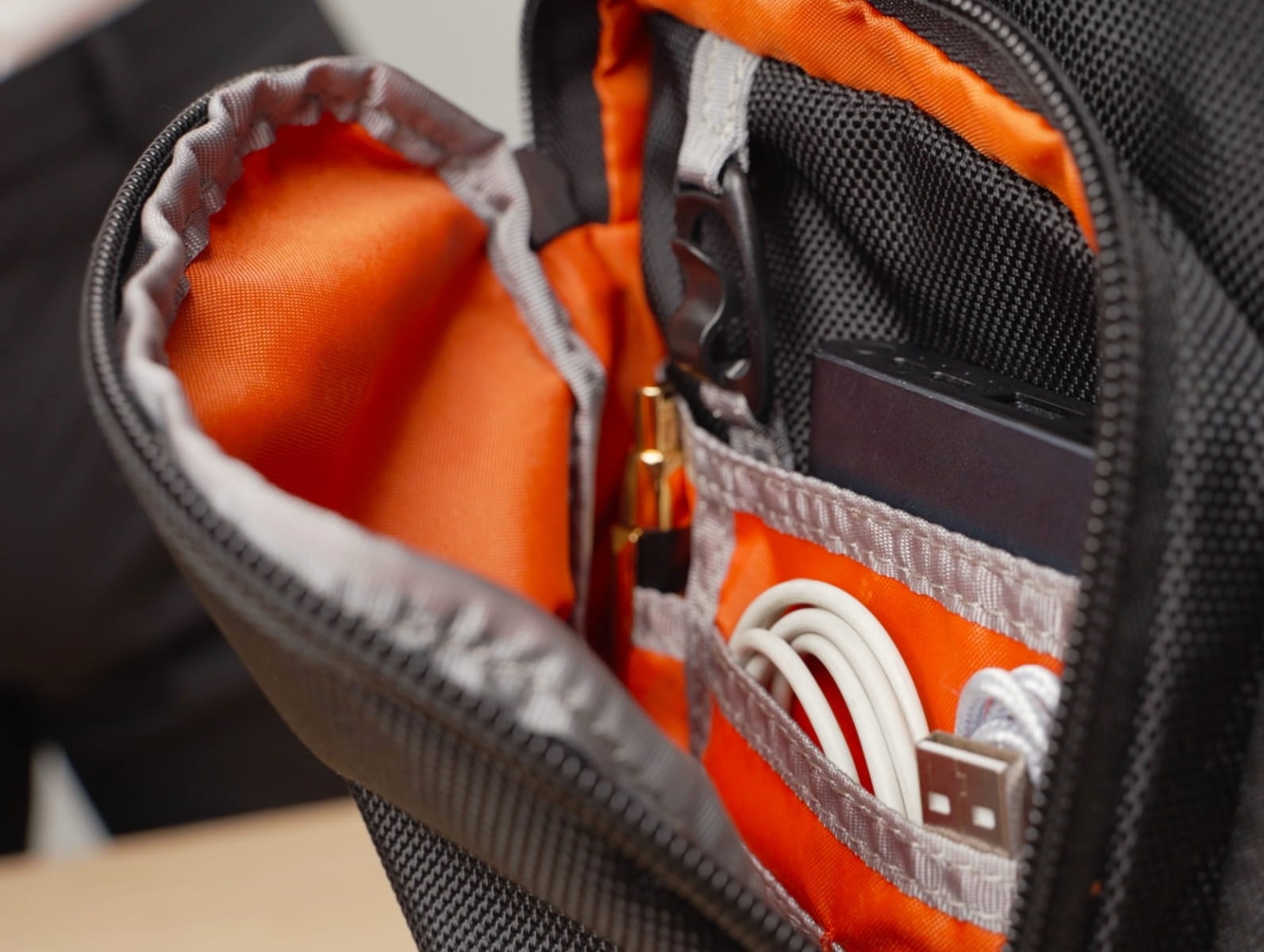 Offenes Laptop-Rucksack-Fach mit orangefarbenem Innenfutter, Netztaschen, Kabeln und einer Powerbank.