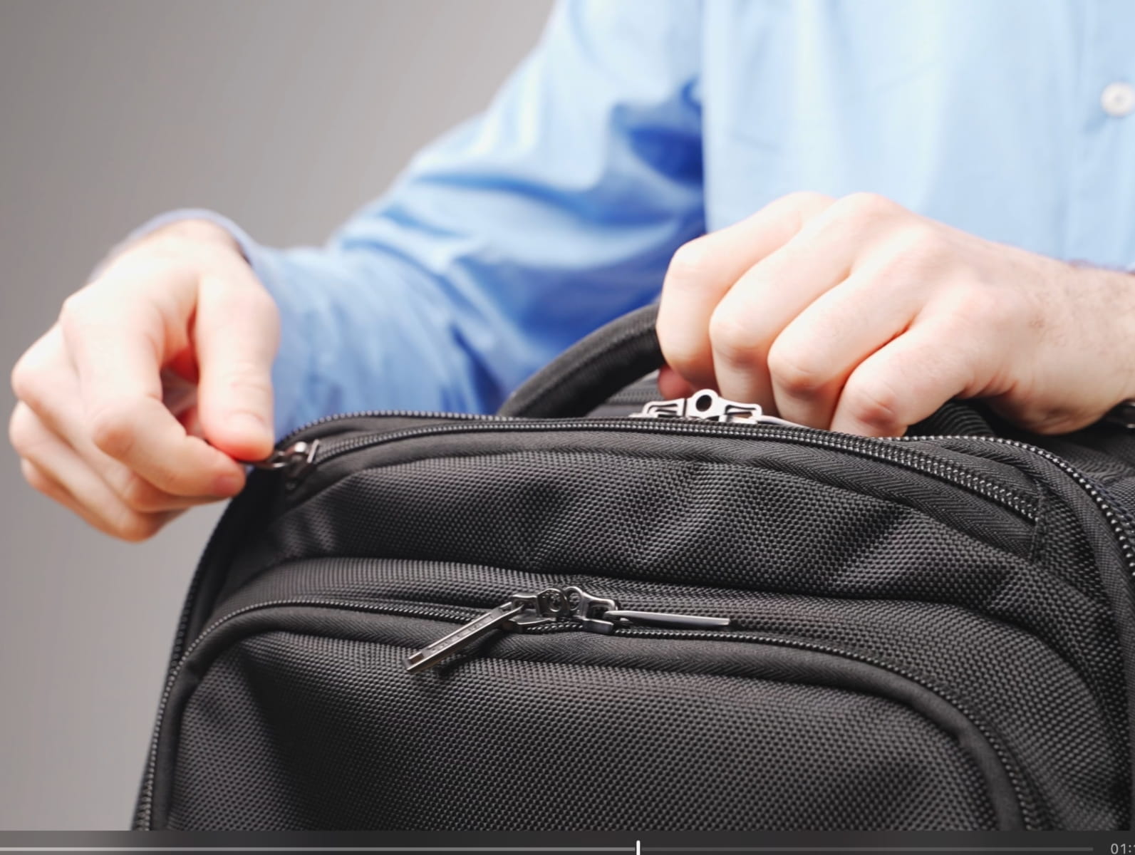 Hände öffnen den Reißverschluss eines schwarzen Laptop-Rucksacks.