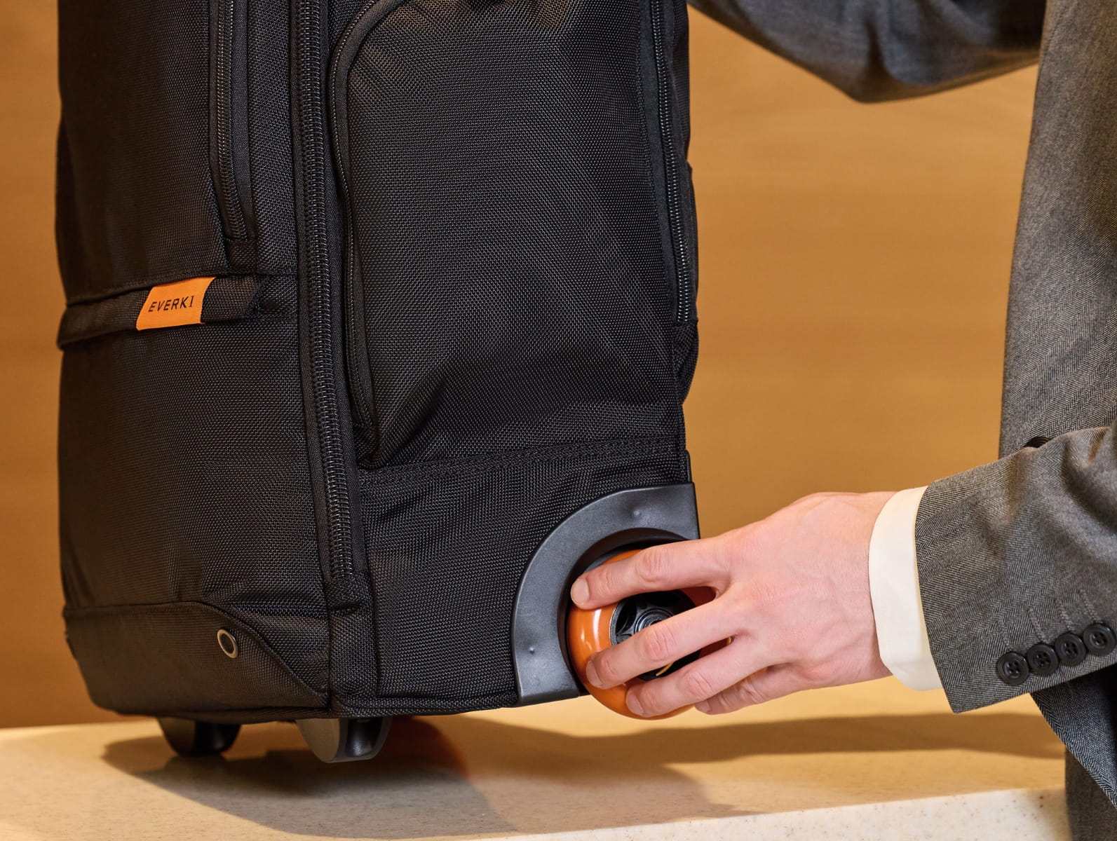 Hand hält die große, orangefarbene Laufrolle eines schwarzen Everki Laptop-Trolleys.