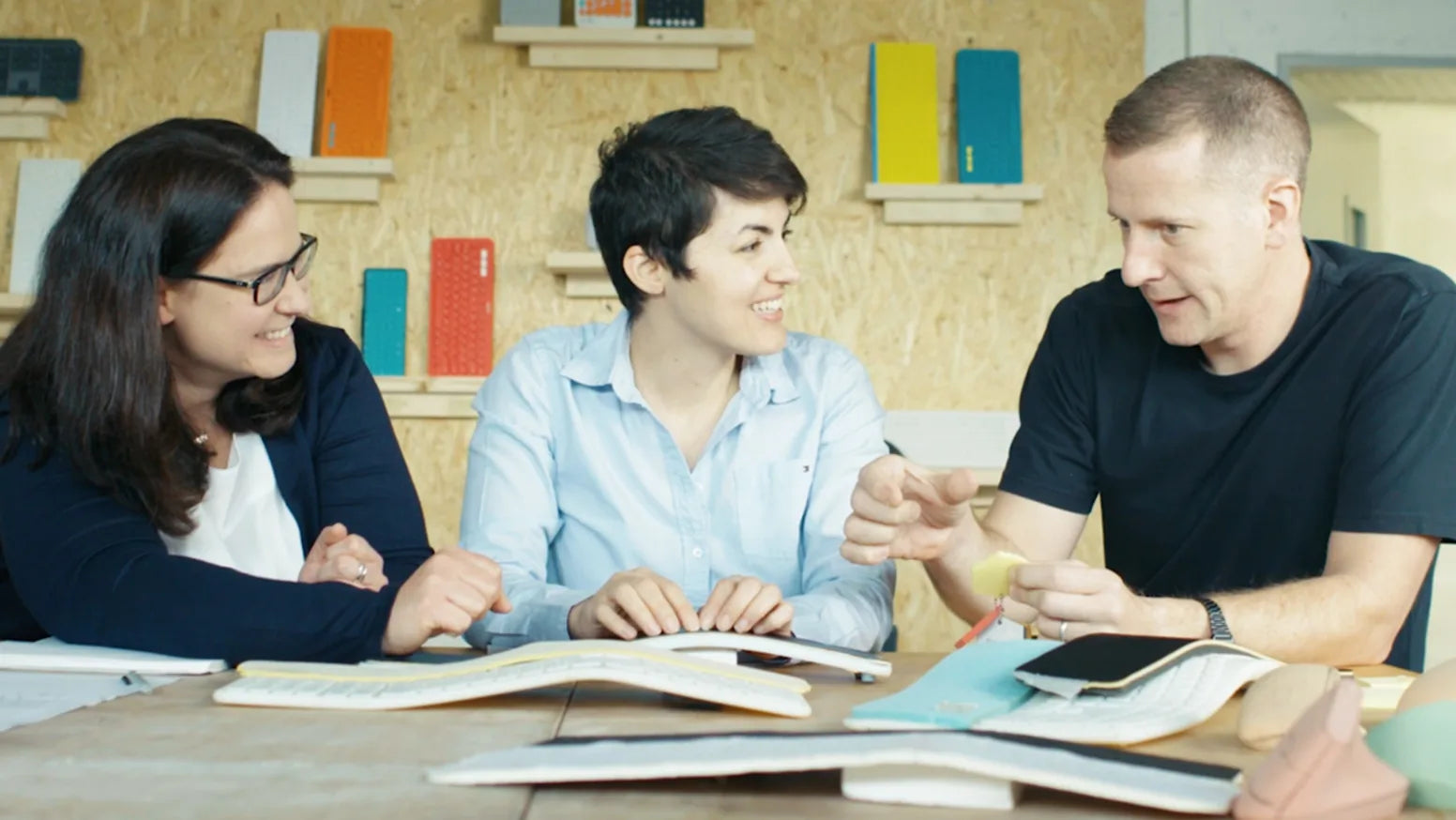 Drei Teammitglieder sitzen an einem Holztisch und besprechen Hardware-Designs in einem modernen Büro.