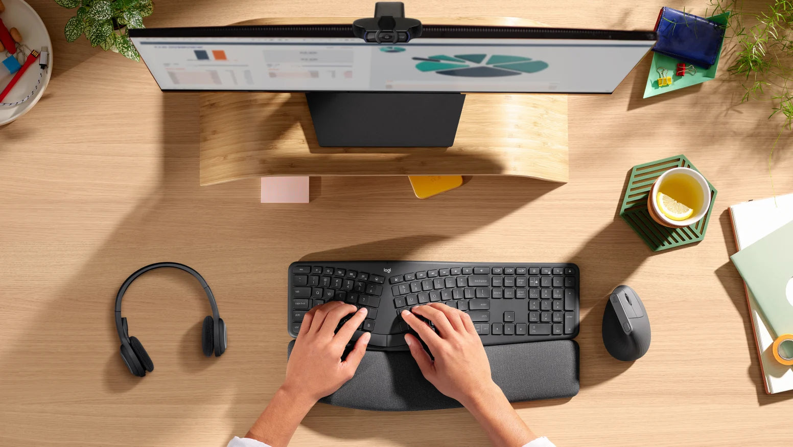 Ergonomischer Holz-Schreibtisch von oben mit Monitor, geschwungener Tastatur, ergonomischer Maus und Kopfhörern.