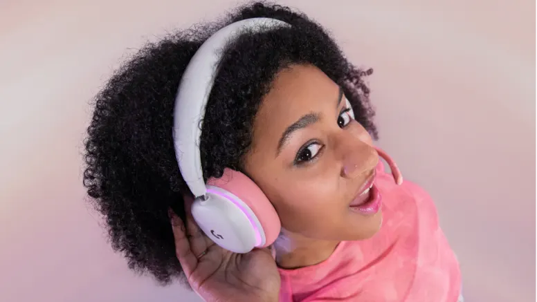 Junge Frau mit dunklen Locken trägt ein weiß-rosafarbenes Gaming-Headset mit Mikrofon