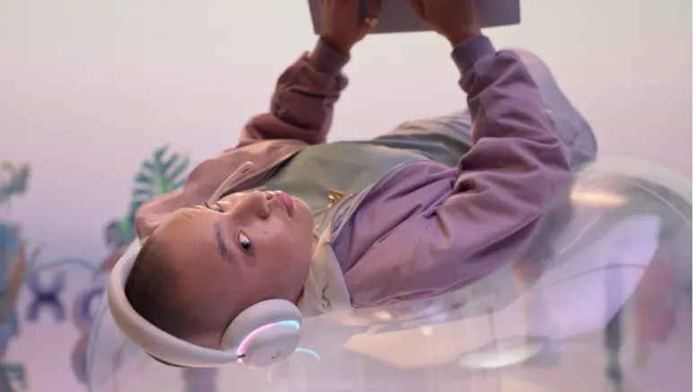 Eine Person liegt entspannt mit Gaming-Headset auf einem transparenten Sessel und bedient einen Laptop