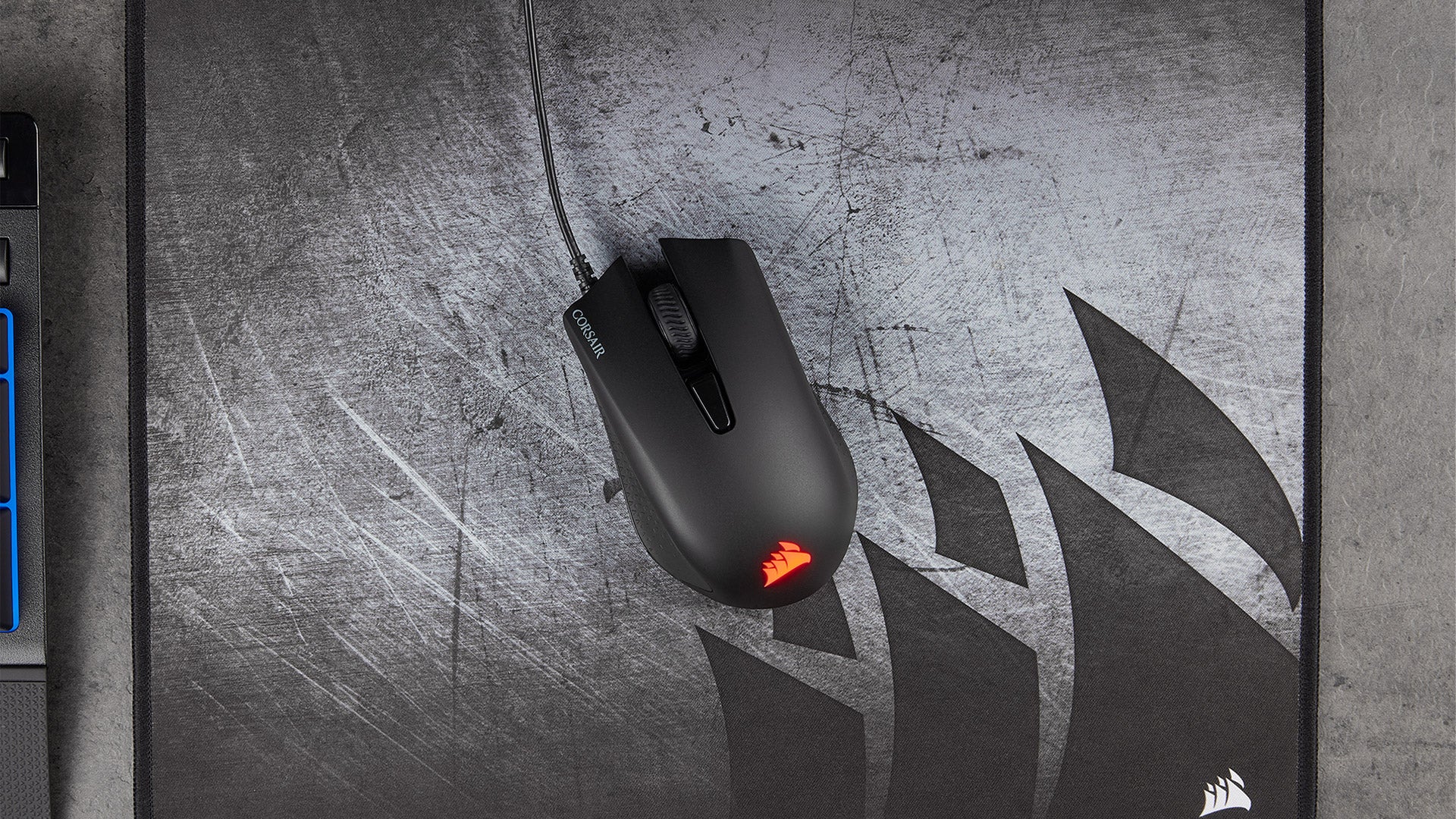 Schwarze Corsair Gaming-Maus mit rotem Logo auf einem großen Mauspad mit grauem Muster