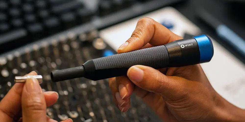 Hände halten einen blauen iFixit Präzisionsschraubendreher beim Wechseln eines Bits.