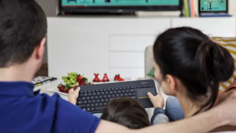 Paar bedient kabellose Logitech-Tastatur mit integriertem Touchpad im Wohnzimmer vor dem Fernseher