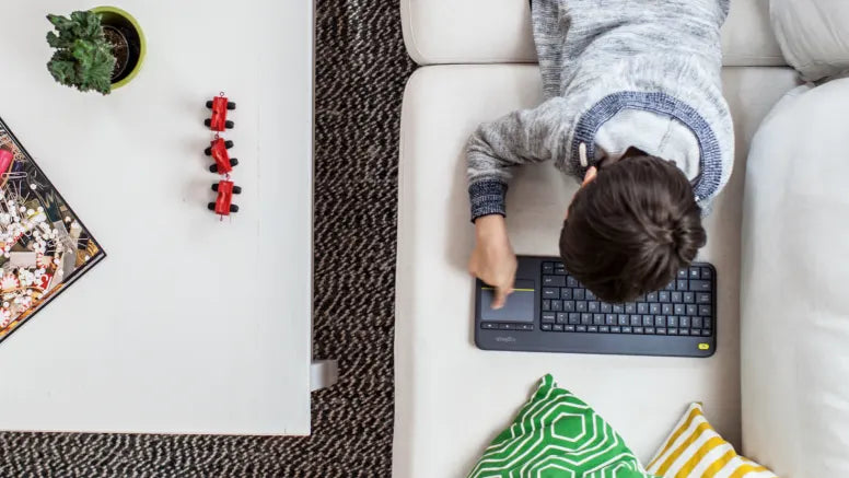 Kind bedient kabellose Logitech-Tastatur mit integriertem Touchpad auf dem Sofa