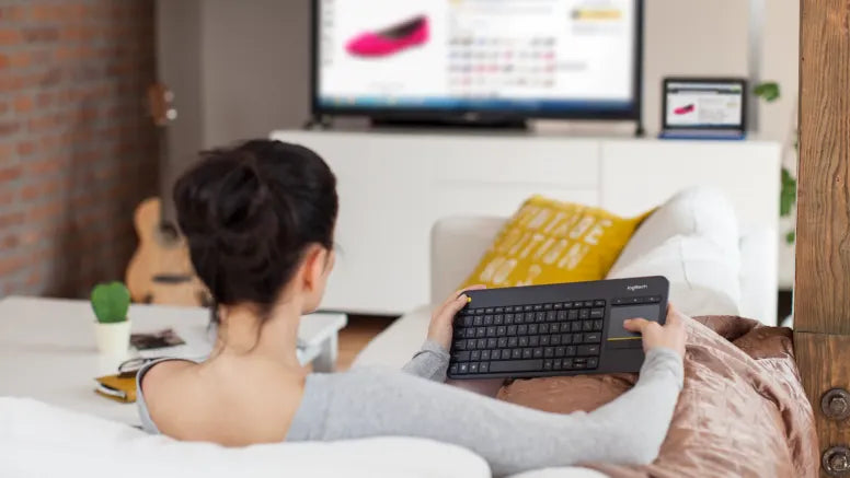 Frau bedient kabellose Logitech Wireless Touch Keyboard mit integriertem Touchpad vom Sofa aus vor Fernseher