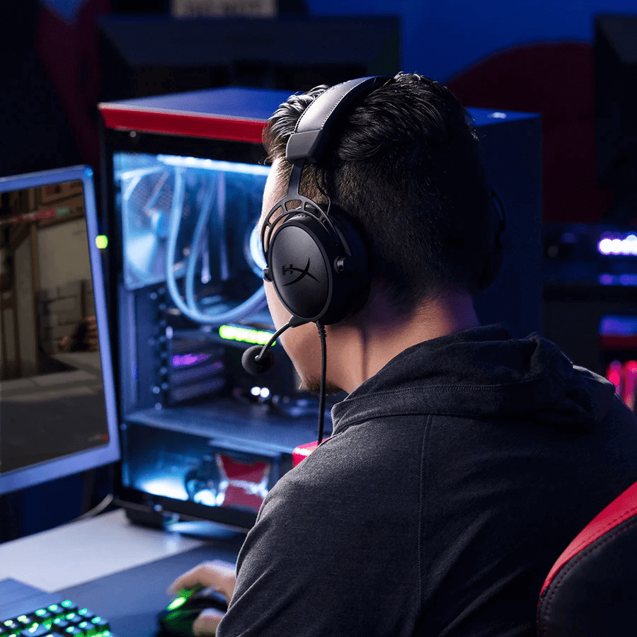Gamer mit Gaming-Headset sitzt vor beleuchtetem High-End PC und Monitor.