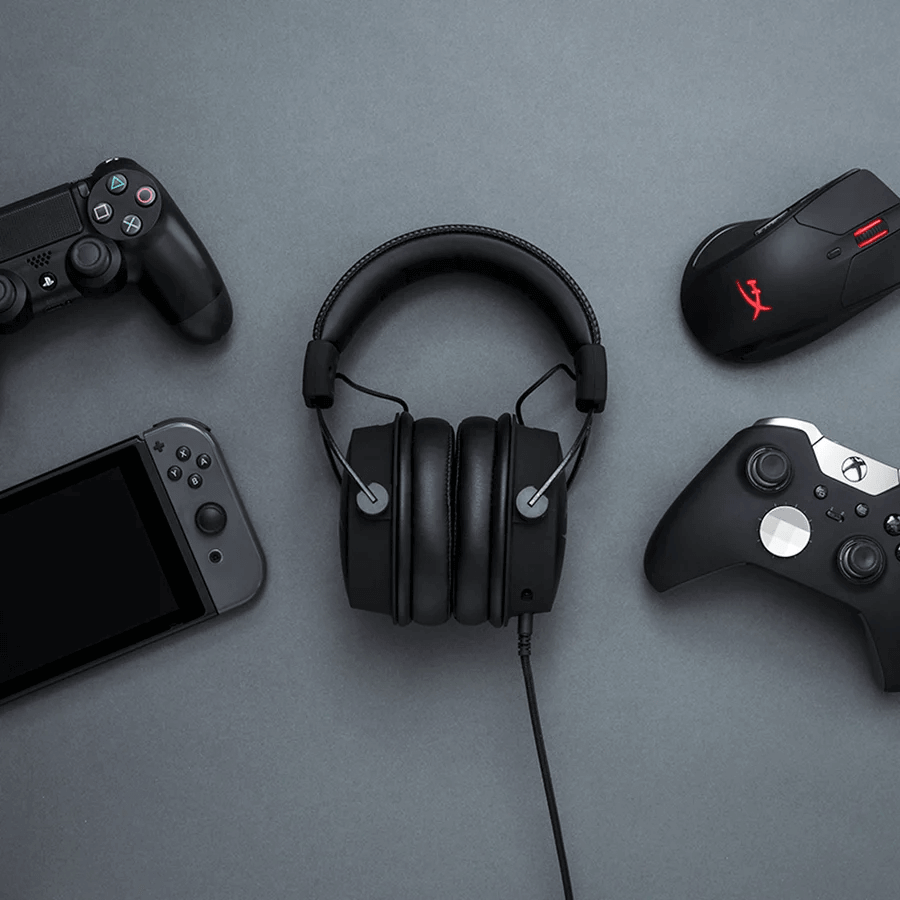 Schwarzes Gaming-Headset im Zentrum, umgeben von Controllern und einer Gaming-Maus auf grauem Untergrund.